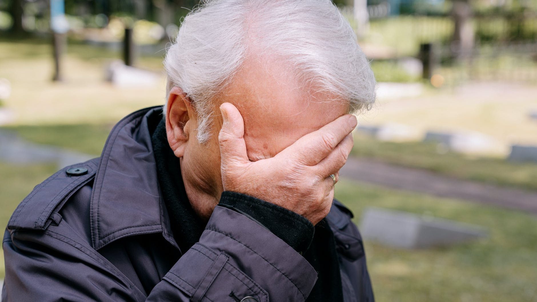 an elderly man covering his face